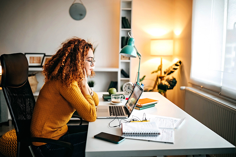 Woman studying at a desk with a laptop, notes, and books.