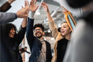 group of young professionals in a circle raising their right arms