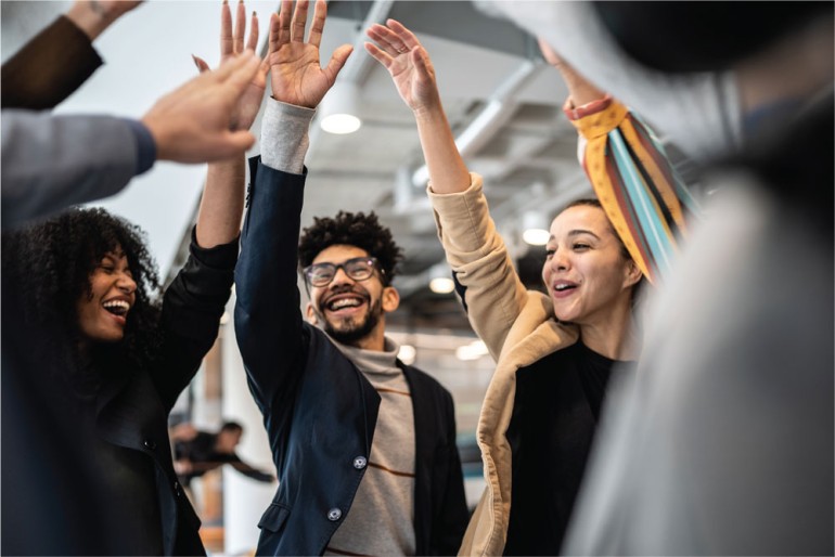 group of young professionals in a circle raising their right arms